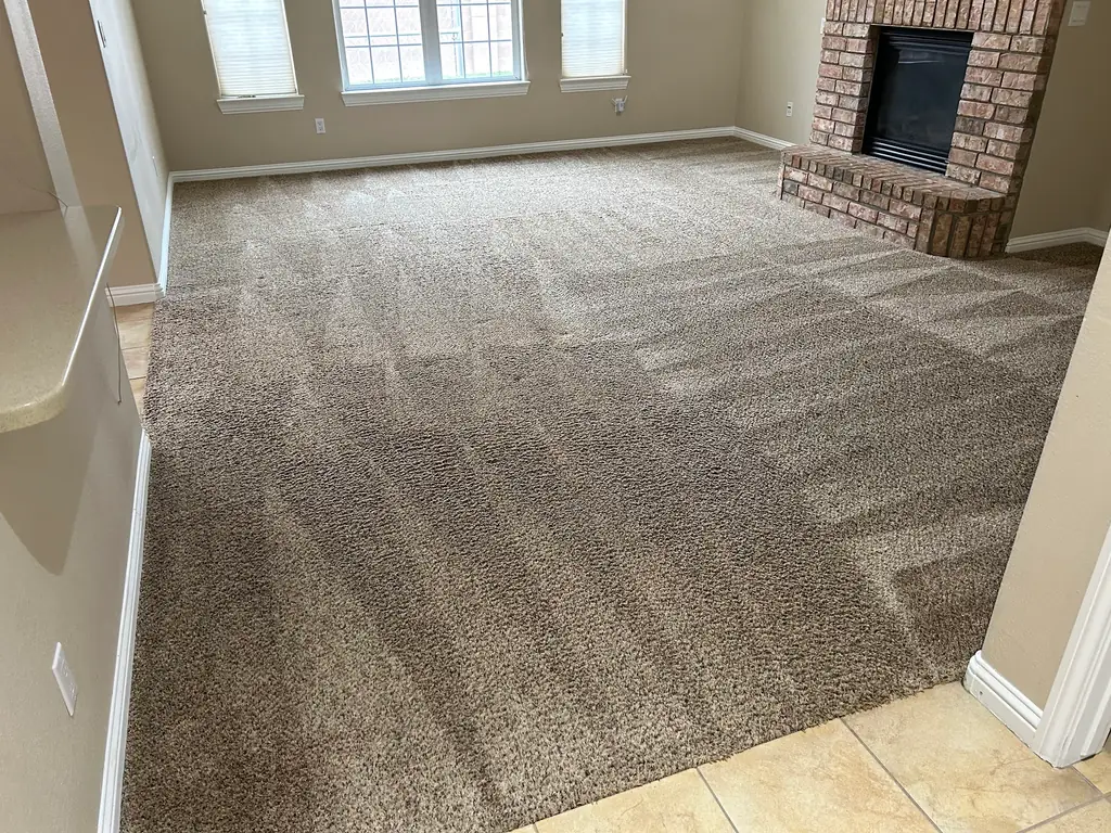 A cleaned Albuquerque living room with a brick corner fireplace and grooming lines visible across the freshly cleaned carpet pile